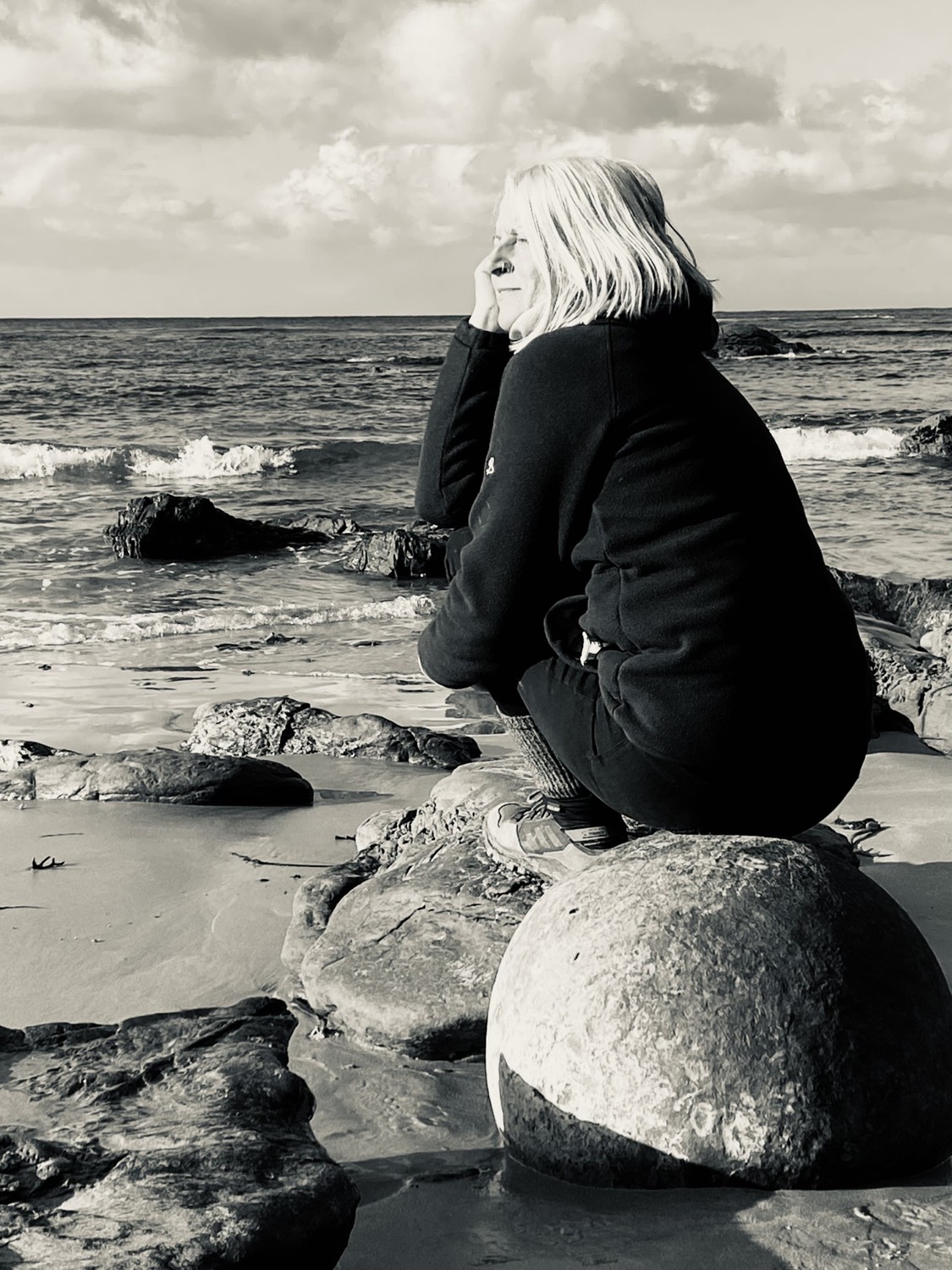 Imogen sitting on a boulder at the water's edge, looking out to sea