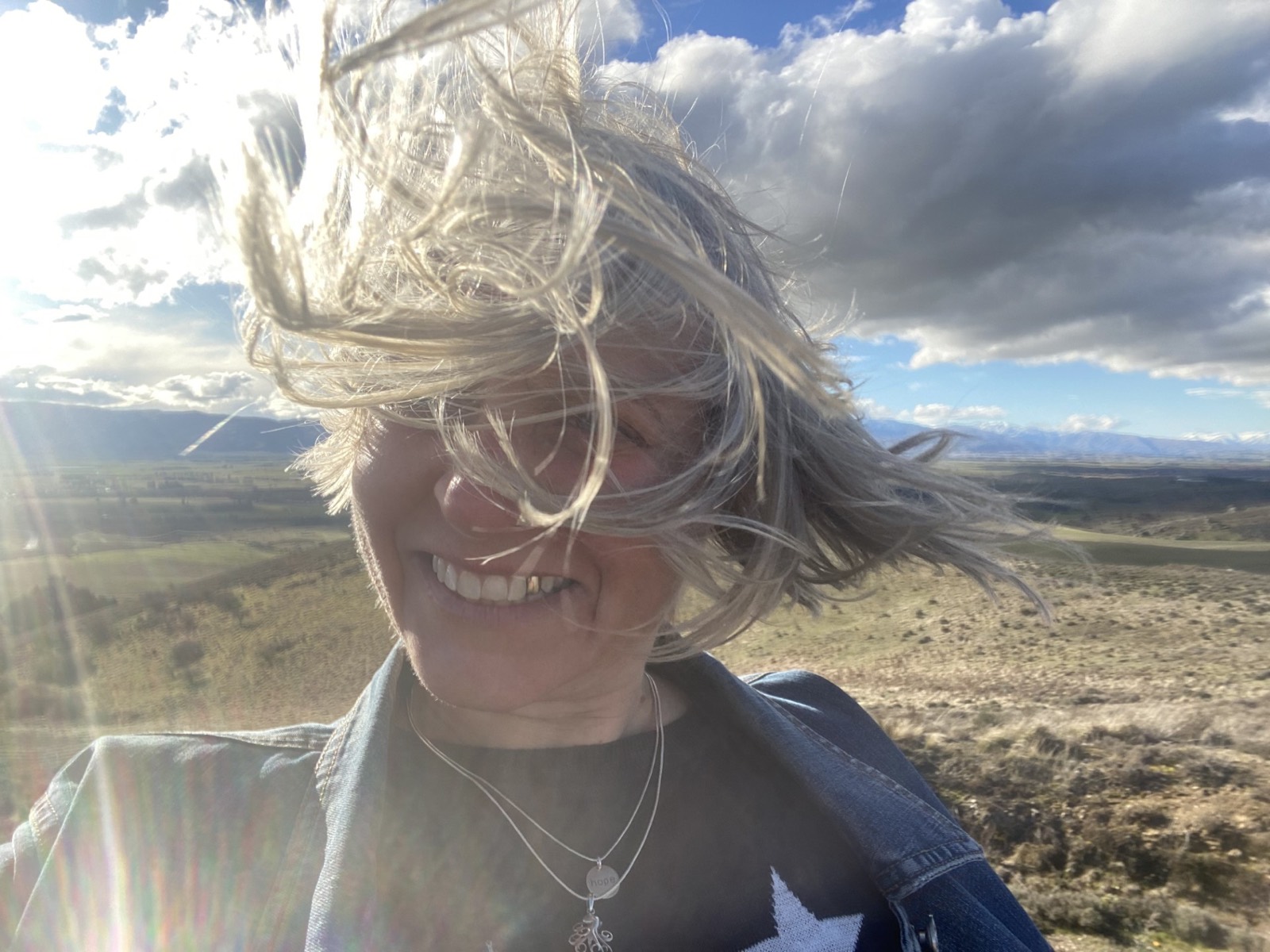 Imogen smiling on a windy hilltop, her hair blowing across her face